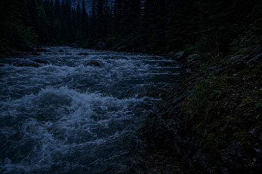 A rapid running river at night surrounded by a dark forest.